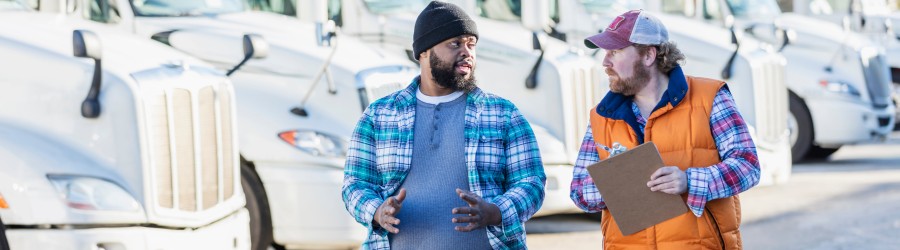 Two truck drivers talking in front of a fleet of semi-trucks