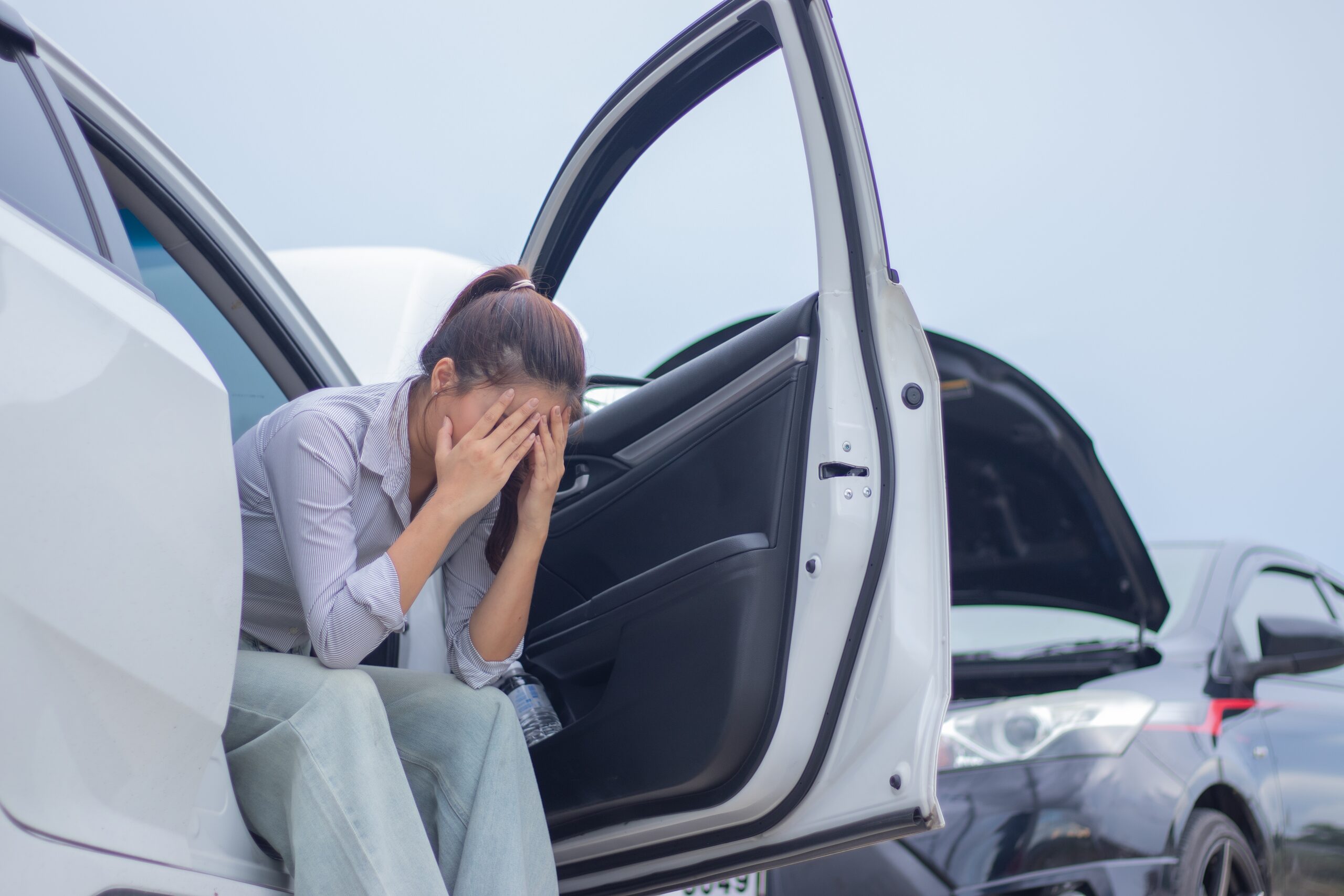 Driver sitting beside damaged vehicle after a Florida car accident while dealing with emotional distress, anxiety, and psychological trauma symptoms