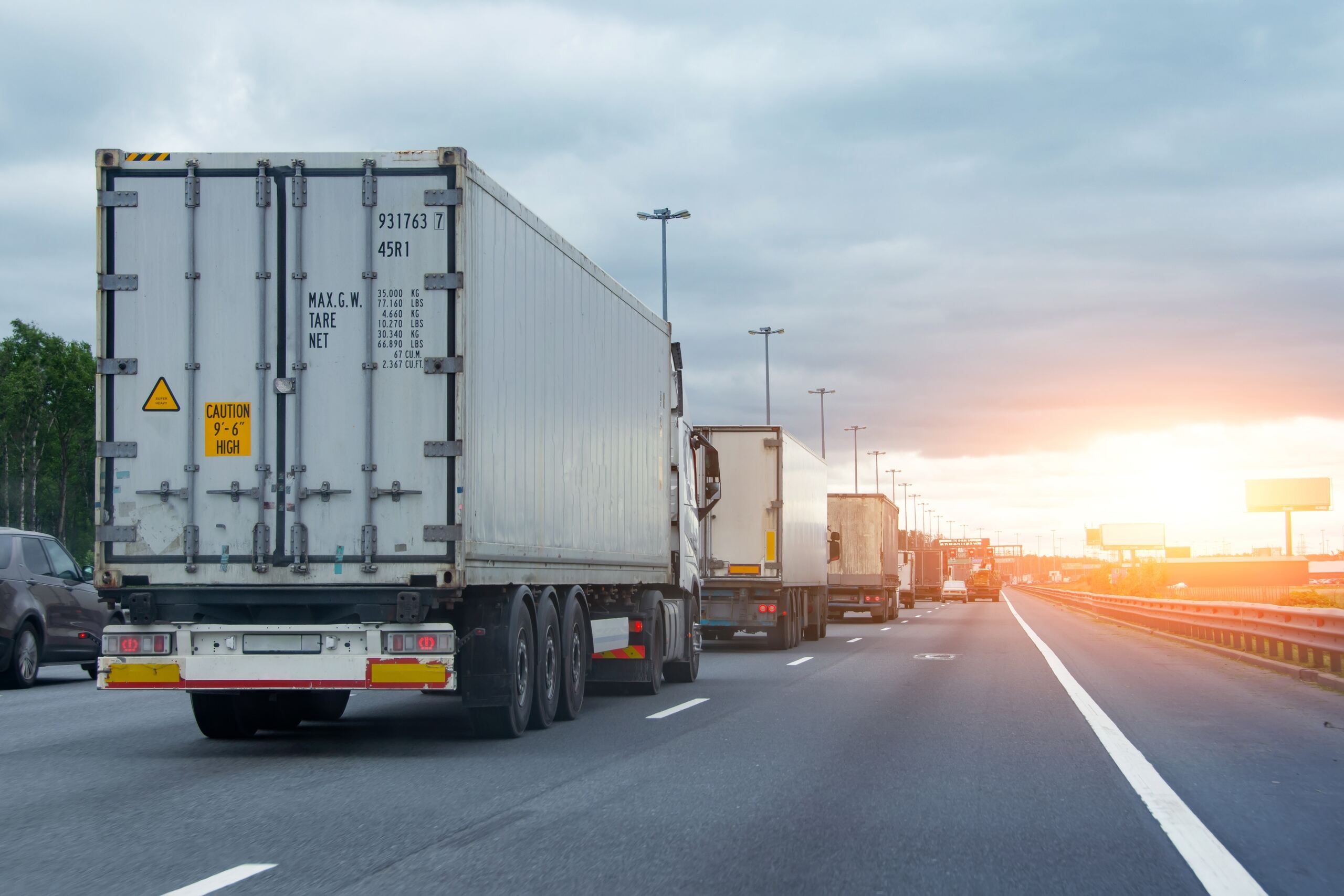 A line of large commercial cargo trucks driving on a multi-lane highway at sunset, representing the heavy commercial traffic handled by Pensacola jackknife truck accident lawyers.